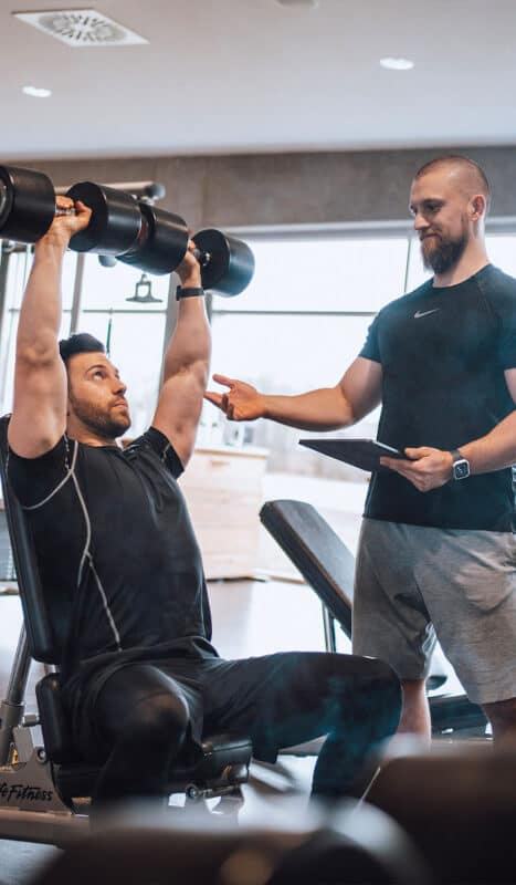 David Bachmeier, professioneller Fitness-Trainer, hilft seinem Kunden beim Muskelaufbau im Fitnessstudio durch effektives Training mit Gewichten.