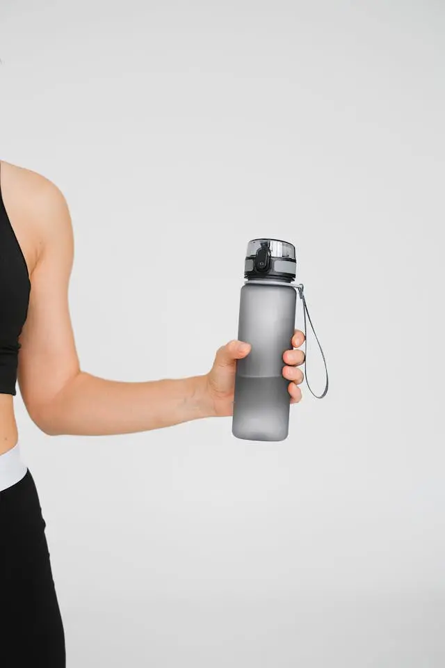 Frau hält während des Trainings zum Muskelaufbau eine graue Wasserflasche hoch.